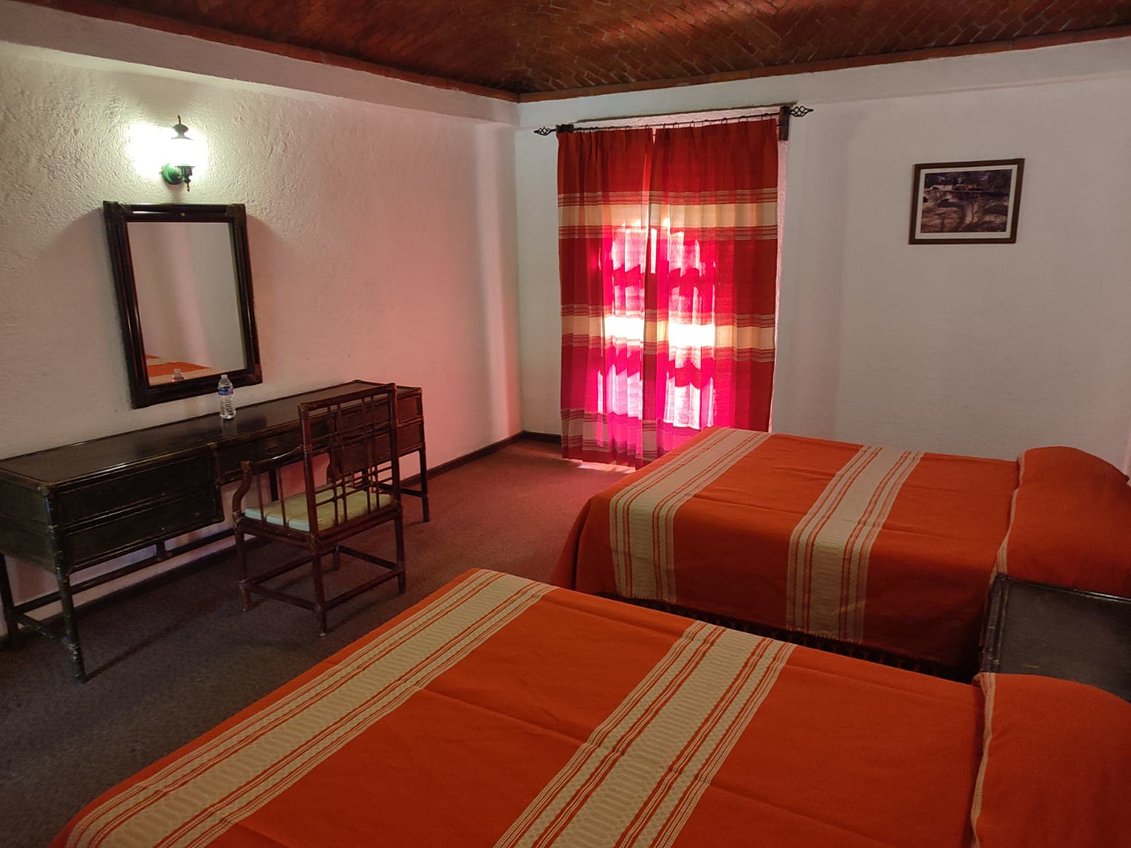 Habitación con dos camas, techo de ladrillo y cortinas rojas